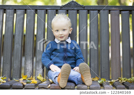 Little boy on a bench in the autumn park. Little boy on a bench in the autumn park. 122840169