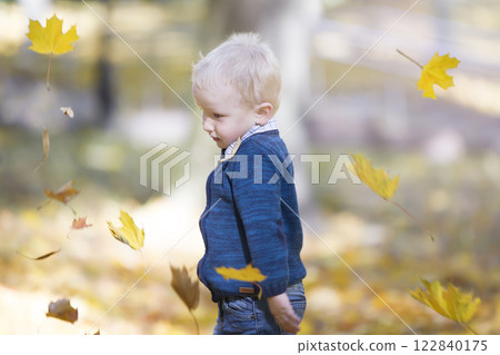 A small child on the background of flying autumn leaves. Boy in autumn park 122840175