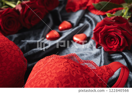 Romantic dating. Valentine's day, lace women's red underwear, lingerie, massage oil and red roses on dark bedclothes. Copy space. Close up. 122840566