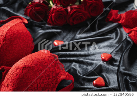 Romantic dating. Valentine's day, lace women's red underwear, lingerie, massage oil and red roses on dark bedclothes. Copy space. Close up. 122840596
