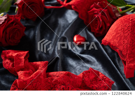 Romantic dating. Valentine's day, lace women's red underwear, lingerie, massage oil and red roses on dark bedclothes. Copy space. Close up. Romantic dating. Valentine's day, lace women's red underwear, lingerie, massage oil and red roses on dark bedclothes. Copy space. Close up. 122840624