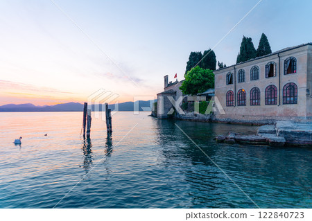 Swans on Garda Lake, Punta San Vigilio, Italy. Sunset view of historic building. 122840723