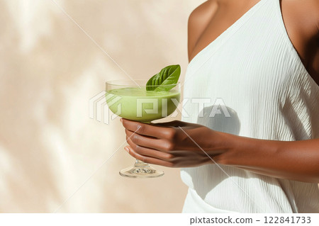 A fit woman holding a fresh green juice in sunlight. The scene evokes health, fitness, and vitality in a minimalist and bright environment 122841733