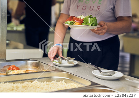 A woman serves a salad of fresh vegetables. Buffet service at the hotel. Offering self-service options, ideal for creating a copyspace image. High quality photo 122842227