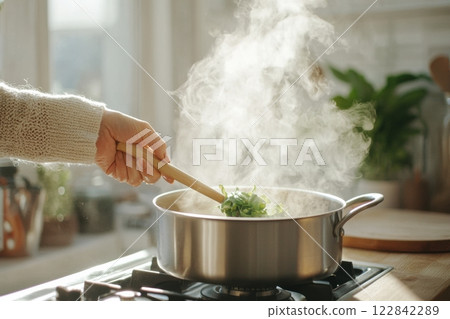 Hand stirrinHand stirring steaming vegetables in a stainless steel pot on a gas stove. Home cooking and healthy food concept.g steaming vegetables in a stainless steel pot on a gas stove. Home cooking 122842289