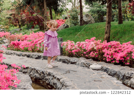 Cute child girl in pink dress walking in blooming garden 122842312