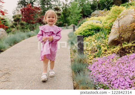 Smiling child girl in pink dress walking in summer blooming garden 122842314