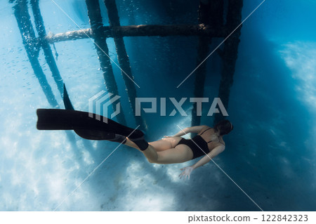 Freediver woman swimming underwater under the pier in blue sea in sunny summer day. 122842323