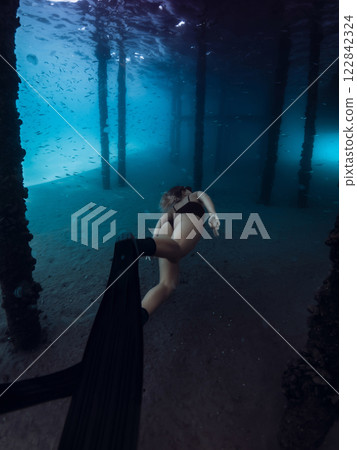 Woman free diver swims underwater on deep in transparent ocean. Freediving under the pier Woman free diver swims underwater on deep in transparent ocean. Freediving under the pier 122842324