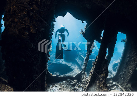 Free diver explores underwater shipwreck, surrounded by light rays and marine growth. Free diving at wreck ship 122842326