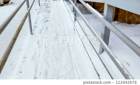 Close-up of a ramp with metal railings, covered with snow, for baby strollers and handicapped accessibility 122842678