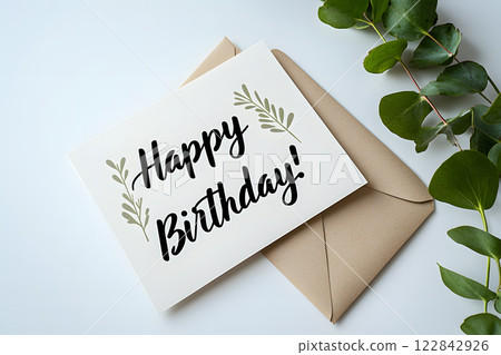 happy birthday card with a minimal botanical design placed on a kraft envelope, accompanied by fresh eucalyptus leaves on a light background 122842926
