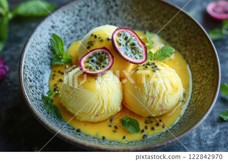 Delicious passion fruit ice cream with mango sauce and mint leaves being served in a ceramic bowl 122842970