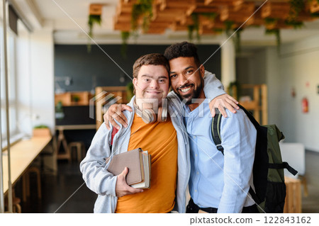 Young man with Down syndrome and his buddy with arms around looking at camera indoors at school 122843162