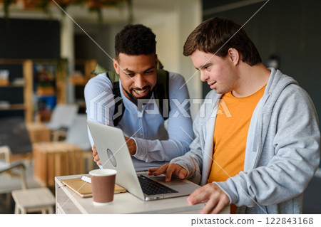 Happy young man with Down syndrome and his tutor using lapotp indoors at school. Happy young man with Down syndrome and his tutor using lapotp indoors at school. 122843168
