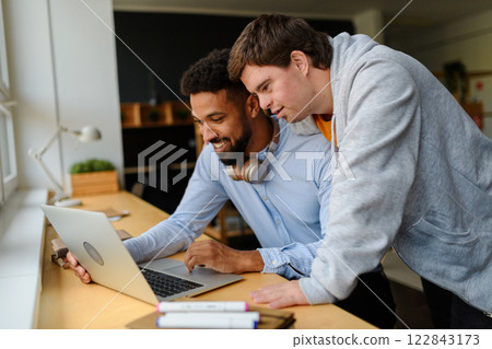 Happy young man with Down syndrome and his tutor using lapotp indoors at school. Happy young man with Down syndrome and his tutor using lapotp indoors at school. 122843173