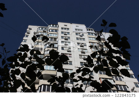 Dark Branches Of Bushes Against The Background Of A Brick High Rise Apartment Building In The Early Morning. First Sun Rays On A Building At Dawn Time  122843175