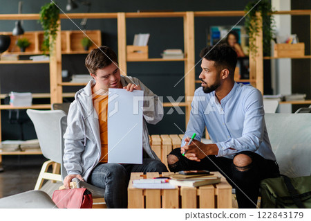 Young man with Down syndrome studyng with special educator teacher in special education classroom. Young man with Down syndrome studyng with special educator teacher in special education classroom. 122843179