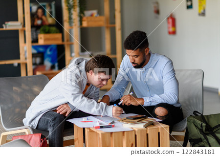 Young man with Down syndrome studyng with special educator teacher in special education classroom. Young man with Down syndrome studyng with special educator teacher in special education classroom. 122843181