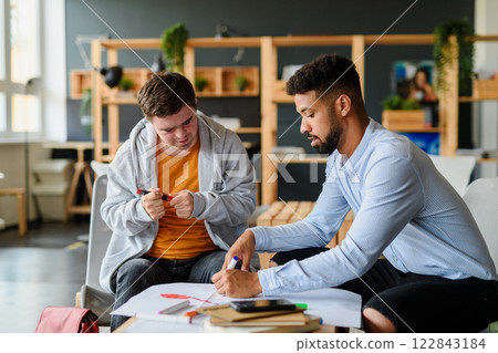 Young man with Down syndrome studyng with special educator teacher in special education classroom. 122843184