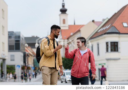 A young man with Down syndrome and his mentoring friend walking across city, talking. A young man with Down syndrome and his mentoring friend walking across city, talking. 122843186
