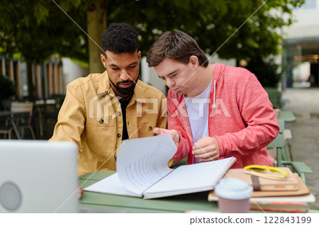 Young man with Down syndrome studyng with special educator teacher. Young man with Down syndrome studyng with special educator teacher. 122843199