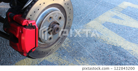 Detailed photo to illustrate the structure of a car brake disc and caliper with copy space. Brake disc and brake pads inside red caliper on asphalt background  122843200