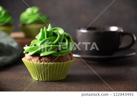 St. Patrick's Day coffee and homemade cupcakes with green whipped cream and chocolate sprinkles on brown background. Close up. 122843491