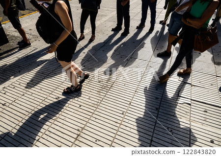 A group of people on a sidewalk with shadows on the ground 122843820
