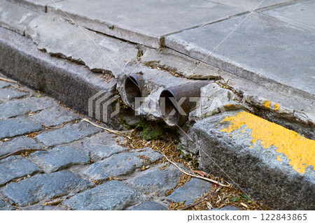 A broken pipe is currently resting on the side of a cobblestone street 122843865