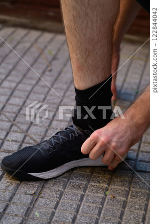 A man is crouched down, carefully tying his shoes on a tiled floor A man is crouched down, carefully tying his shoes on a tiled floor 122844042