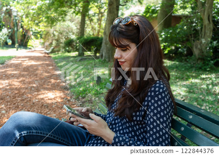 Young woman using smartphone sitting on bench in park 122844376