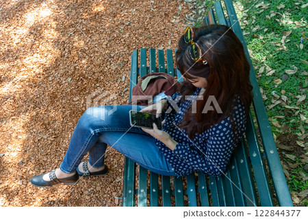 Young woman using smartphone while relaxing on park bench 122844377