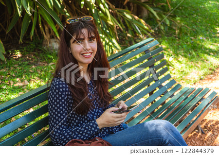 Young woman using smartphone while relaxing on park bench Young woman using smartphone while relaxing on park bench 122844379