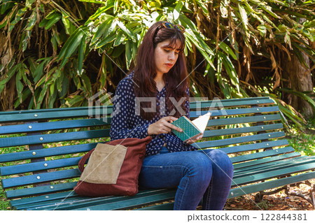 Young woman reading book while sitting on bench in park 122844381