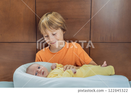 A young boy lovingly holds his newborn brother in a cozy sleep cocoon, sharing a tender sibling moment. A heartwarming scene of family bonding, protection, and the start of a lifelong brotherly 122845322