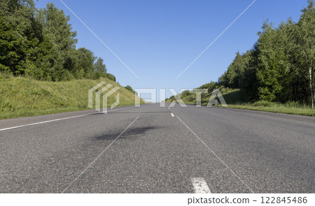 an empty straight paved road against a blue sky background an empty straight paved road against a blue sky background 122845486