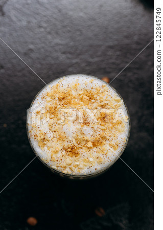 Layered latte with frothy milk and crushed nuts in crystal glass with coffee beans on dark table Layered latte with frothy milk and crushed nuts in crystal glass with coffee beans on dark table 122845749
