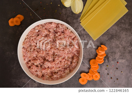 Top view raw ground minced meat in white bowl. Lasagne pasta sheets, onion, carrot, pepper. Black background. Homemade lasagna cooking preparation Top view raw ground minced meat in white bowl. Lasagne pasta sheets, onion, carrot, pepper. Black background. Homemade lasagna cooking preparation 122846165