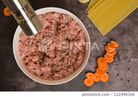 Top view raw ground minced meat in white bowl, pepper mill. Lasagne pasta sheets, carrot, pepper. Black background. Homemade lasagna cooking preparation Top view raw ground minced meat in white bowl, pepper mill. Lasagne pasta sheets, carrot, pepper. Black background. Homemade lasagna cooking preparation 122846166