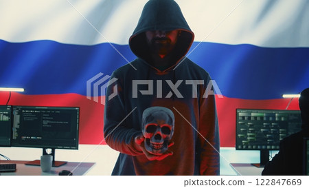 Russian hackers creating dark web maniac cybercrime in a control room, sinister man holding a skull hinting at death threats. Aggressive harmful criminal activity, cyber terrorism. Camera B. 122847669