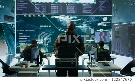 Military expert in a control center uses advanced technology and gear to gather intelligence from satellite imagery and surveillance systems. Using laptop to communicate information. Camera B. Military expert in a control center uses advanced technology and gear to gather intelligence from satellite imagery and surveillance systems. Using laptop to communicate information. Camera B. 122847670