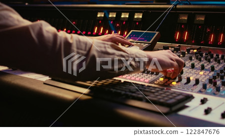Sound designer working with sliders and switchers on control desk in professional music recording studio, editing and producing songs for a new album. Technician adjusting volume levels. Camera B. Sound designer working with sliders and switchers on control desk in professional music recording studio, editing and producing songs for a new album. Technician adjusting volume levels. Camera B. 122847676