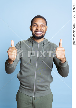 Happy pleased young man giving like sign in front of the camera, posing with positive vibes and shows agreement. African american person gives thumbs up in studio, relaxed lively guy. Happy pleased young man giving like sign in front of the camera, posing with positive vibes and shows agreement. African american person gives thumbs up in studio, relaxed lively guy. 122847690