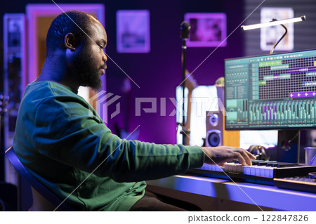 Musician playing piano keyboard and recording tracks for mix and master session, using digital software on pc to create new songs. Sound producer composing music with midi controller tool. Musician playing piano keyboard and recording tracks for mix and master session, using digital software on pc to create new songs. Sound producer composing music with midi controller tool. 122847826