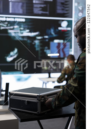 Army soldier handles satellite radar real time data on laptop in command post, coordinates strategic missions to support national defense operations in a high tech military base. Close up. Army soldier handles satellite radar real time data on laptop in command post, coordinates strategic missions to support national defense operations in a high tech military base. Close up. 122847842