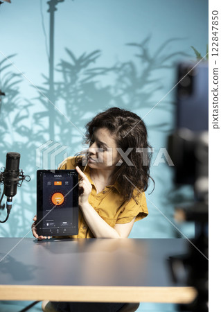Influencer in studio doing affiliate marketing, advertising smart light controlling tablet application for online streaming platforms. Content creator promoting IoT home automation product tech 122847850