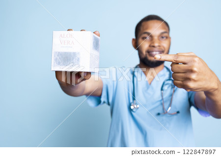 Portrait of dermatologist talking about refreshing aloe vera gel, standing against blue background. Skincare expert recommending detox anti inflammatory beauty moisturizer, organic lotion. 122847897