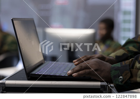 IT professional operating laptop to gather important information from cctv satellite systems, control tower tasks. Collecting real time data for security measures and national interests. Close up. 122847898