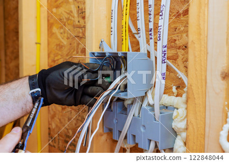 Electrician connects wires inside circuit box while renovating home, ensuring proper electrical setup 122848044